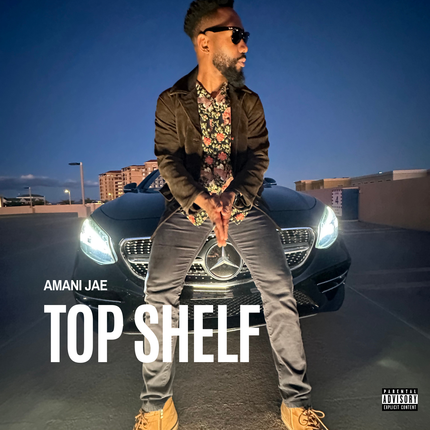 Cover photo of Amani Jae's new single Top Shelf with Amani standing in front of a black car wearing brown boots, grey jeans, brown jacket, and dark sunglasses.